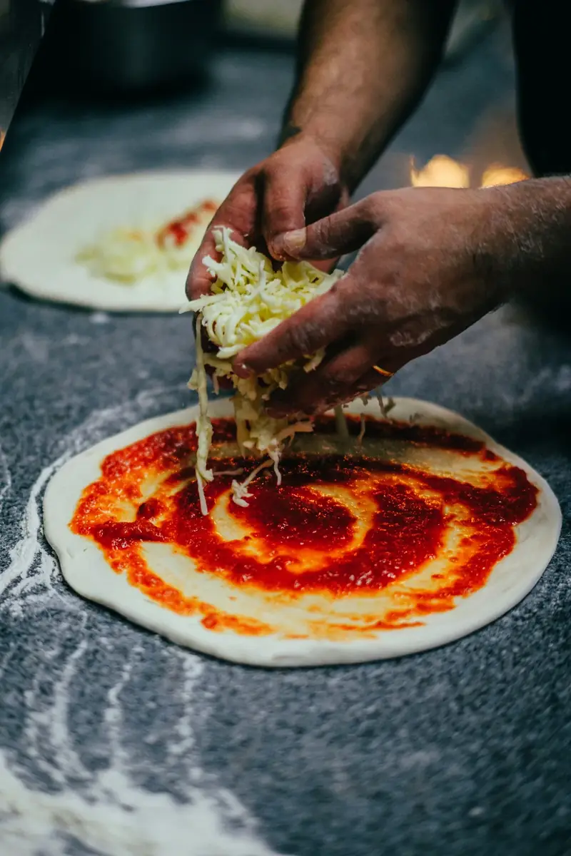 Pizzero agregando salsa y queso sobre masa artesanal