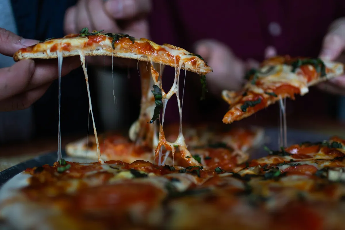 Manos tomando porciones de pizza con queso derretido