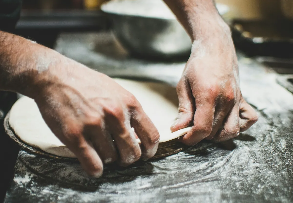 Manos estirando masa de pizza artesanal sobre mesa enharinada